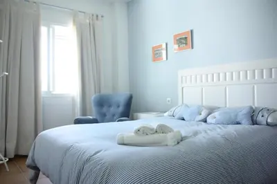 a bedroom with a white bed with a blue chair at Apartamento Costa Ballena Playa y Golf in Cádiz