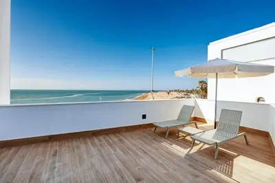 a balcony with two chairs and an umbrella and the ocean at Sercotel Cruz Del Mar in Chipiona