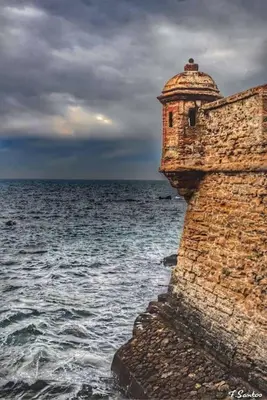 a brick wall next to the ocean with a cloudy sky at A 5 min de la playa Victoria y del Htal Pta Mar in Cádiz