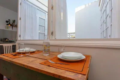 a wooden table with plates and glasses and a window at Wehostcostaluz EL NIDO GADITANO in Cádiz