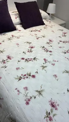 a bed with a white comforter with pink flowers on it at Apartamento Castillo San Marcos in El Puerto de Santa María