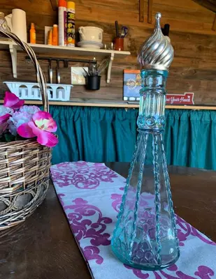 a glass bottle on a table with a basket of flowers at La via de la Yurta in Cádiz