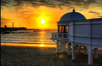 a building on the beach with a sunset in the background at Casa Parque Genovés junto a la playa in Cádiz