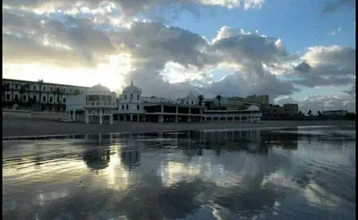 a group of buildings on a beach with a reflection in the water at Casa Parque Genovés junto a la playa in Cádiz