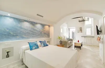a bedroom with a white bed and a painting on the wall at La Cueva del Corregidor in Arcos de la Frontera