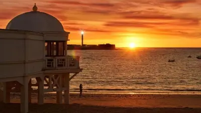 a building on the beach with a sunset at Le Charme Little Apartments in Cádiz