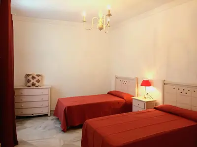 a bedroom with two beds with red sheets and a chandelier at Casa de los Patios in Sanlúcar de Barrameda