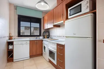 a kitchen with white appliances and wooden cabinets at Golden Sands Apartment - Chiclana de la frontera in Novo Sancti Petri