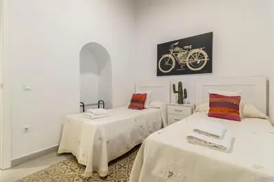 two beds in a white room with a bike on the wall at Apartamento Santa Clara 1 in Jerez de la Frontera