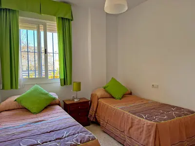 two beds in a room with green curtains and a window at Apartamento Albatros - Ole Solutions in Sanlúcar de Barrameda