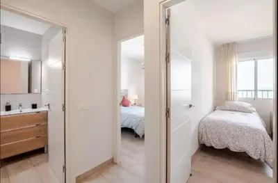 a white bedroom with a bed and a bathroom at Piso Cádiz Playa Victoria in Cádiz