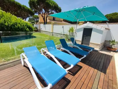 a group of blue lounge chairs and an umbrella on a deck at Villa con piscina junto a la playa in Roche