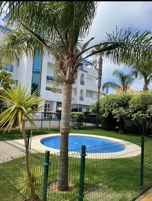 a fence with a palm tree in front of a building at Apartamento en Playa Ballena III in Rota