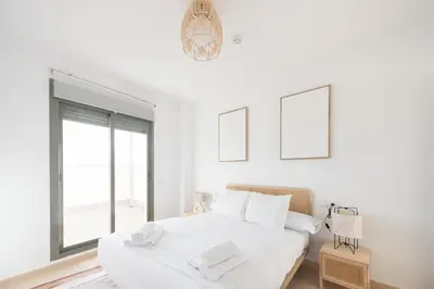 a white bedroom with two beds and a window at APARTOYOU Apartments - Oasis El Puerto in El Puerto de Santa María