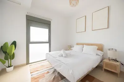 a white bedroom with a bed and a plant at APARTOYOU Apartments - Oasis El Puerto in El Puerto de Santa María