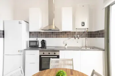 a kitchen with white cabinets and a wooden table at APARTOYOU Apartments - Oasis El Puerto in El Puerto de Santa María