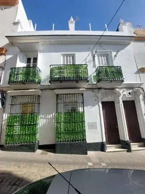 a white house with green gates on the side of it at Casa Madre Gelart Patrimonio Gaditano del siglo XIX in San Fernando
