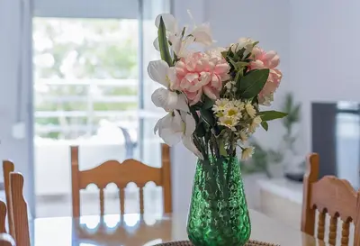 a green vase filled with flowers on a table at Apartamentos Collado Playa Valdelagrana in El Puerto de Santa María