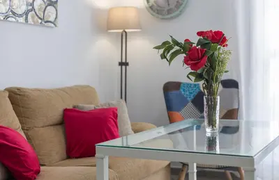 a living room with a glass table with a vase of roses at Apartamentos Collado Playa Valdelagrana in El Puerto de Santa María