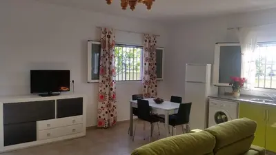 a living room with a table and a kitchen at LOFT Ajardinado en Roche CONIL in Conil de la Frontera