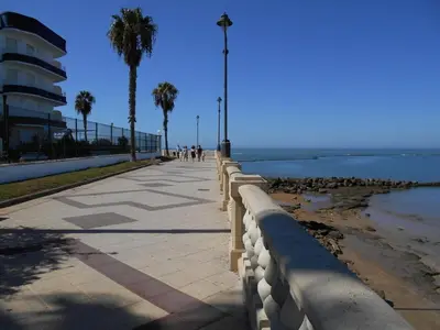 a sidewalk next to the beach with palm trees and a building at Apartamento Caracola Comfortable holiday residence in Chipiona