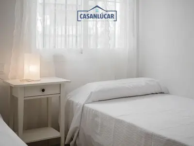 a white bedroom with a bed and a table with a lamp at Carmen Viejo bajo in Sanlúcar de Barrameda