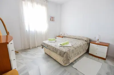 a bedroom with a bed and a dresser and a window at Costa Ballena - Apt para 6 con piscina, terraza, WiFi y parking gratis in Rota