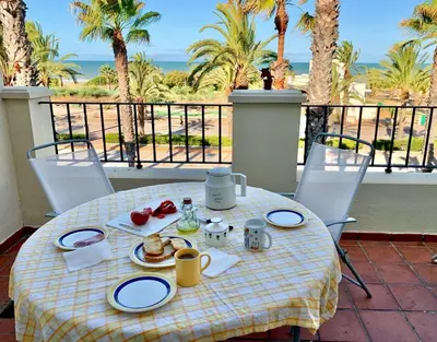 a table with breakfast food on a balcony with palm trees at Costa Ballena - Apt para 6 con piscina, terraza, WiFi y parking gratis in Rota