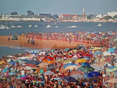a crowd of people on a beach with umbrellas at Plaza Doctor Barbadillo in Sanlúcar de Barrameda
