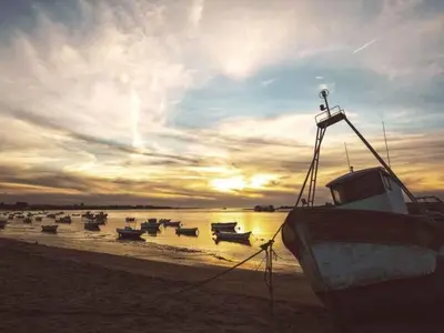 a group of boats sitting on the beach at sunset at Apartamento Cabo Noval in Sanlúcar de Barrameda