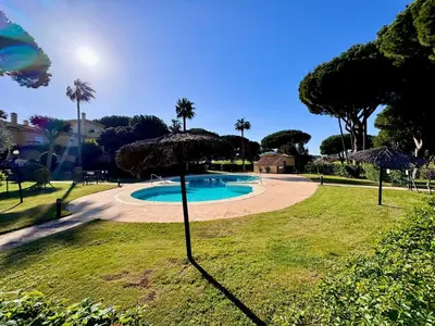 a swimming pool with an umbrella in a park at Precioso Adosado El Cormorán Novo Sancti Petri in Novo Sancti Petri