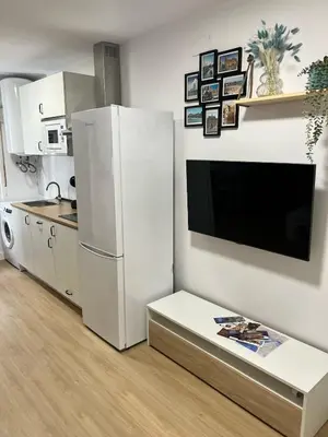 a kitchen with a large white refrigerator and a table at Estudico moderno y cómodo a minutos andando del centro y de la Feria in El Puerto de Santa María