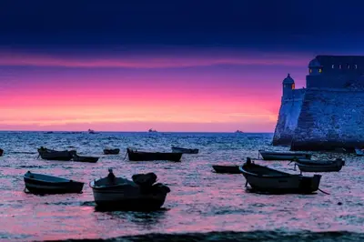 a group of boats in the water with a sunset at Playa La Caleta in Cádiz