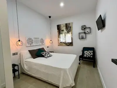 a white bedroom with a bed and a chair at El Refugio in Chiclana de la Frontera