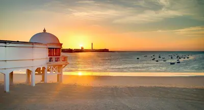a lighthouse on the beach with people in the water at Apartamento Martínez Campos - Playa La Caleta in Cádiz