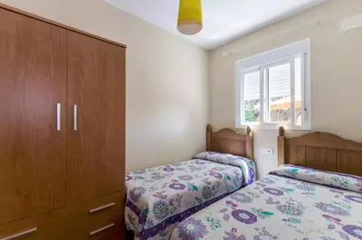 a bedroom with two beds and a cabinet and a window at Turivivienda La Goleta in Conil de la Frontera