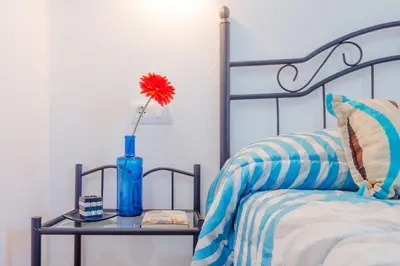 a vase with a red flower on a table next to a bed at Casa Mariana in Conil de la Frontera