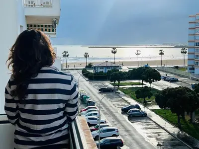 a woman standing on a balcony looking out at the beach at Mi casa vacacional en Valdelagrana in El Puerto de Santa María