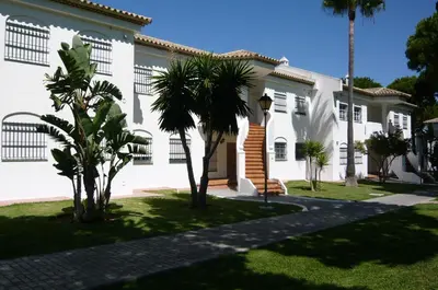 a white building with palm trees in front of it at Residencial Pinar Atlántico in Novo Sancti Petri