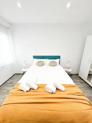 a white bedroom with a large bed with orange blanket at Apartamento La Sal Centro in San Fernando