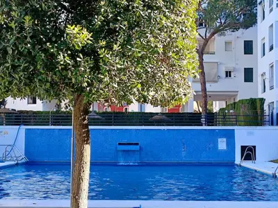 a tree in front of a blue wall and a building at Anc14 Apartamento con 2 habitaciones, patio y piscina al lado de la playa in El Puerto de Santa María