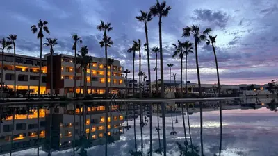 a swimming pool with palm trees and a sunset at Hotel Punta Bermeja Premium in El Puerto de Santa María