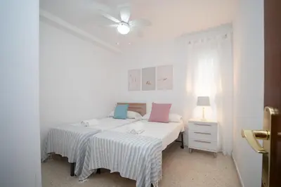 a white bedroom with two beds and a ceiling fan at SIBS Sanlúcar Camelias-Ideal Familias Cerca Playa in Sanlúcar de Barrameda