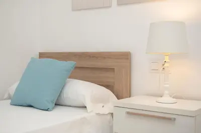 a bed with a blue pillow and a lamp on a night stand at SIBS Sanlúcar Camelias-Ideal Familias Cerca Playa in Sanlúcar de Barrameda