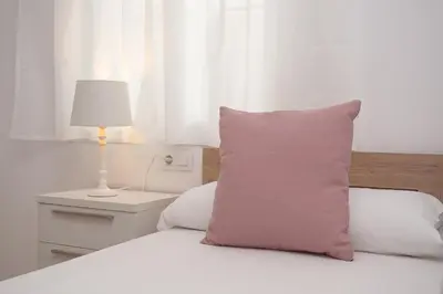 a white bed with a pink pillow and a lamp at SIBS Sanlúcar Camelias-Ideal Familias Cerca Playa in Sanlúcar de Barrameda