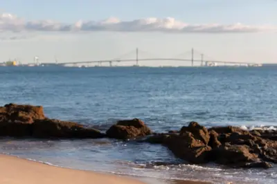 a beach with rocks in the water with a bridge in the distance at Gallery Vistahermosa in El Puerto de Santa María