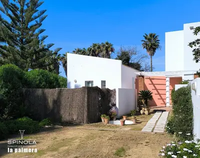 a white house with a fence and palm trees at Spinola Beachfront Bungalows - Apartamentos bungalow en primera linea de playa en Sanlúcar de Barrameda in Sanlúcar de Barrameda
