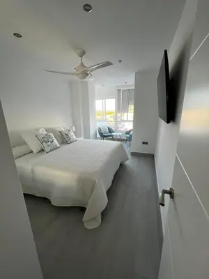 a white bedroom with a bed and a ceiling fan at Apartamento Arena y sal in El Puerto de Santa María