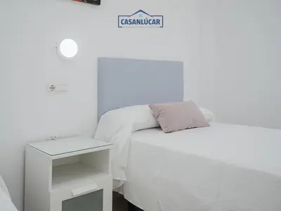 a white bedroom with a bed and a night stand at Piso Real Fernando in Sanlúcar de Barrameda