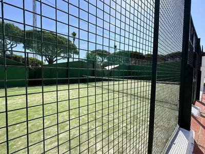 a tennis court seen through a tennis court net at La Almadraba segunda Pista in Chiclana de la Frontera